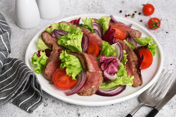 Salad with beef, lettuce and tomatoes on a concrete background.