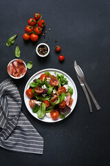 Green salad with prosciutto and blue cheese, on a black dark background with tomatoes
