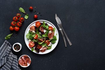 Green salad with prosciutto and blue cheese, on a black dark background with tomatoes
