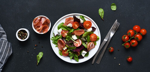 Green salad with prosciutto and blue cheese, on a black dark background with tomatoes
