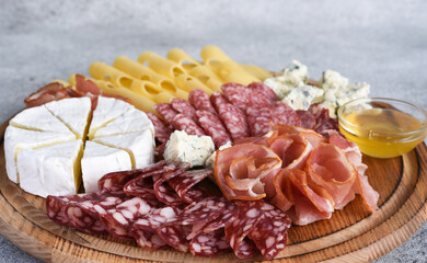 Wooden plate with delicacies. Brie cheese, blue cheese, salami, prosciutto on a wooden board.