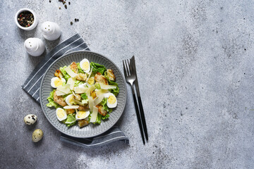 Caesar salad with chicken, sauce, and parmesan on concrete background.