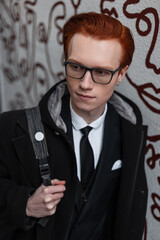 Handsome businessman redhead guy in fashionable clothes with shirt, tie and coat with backpack near wall on the street
