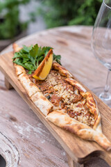 Boat-shaped Flatbread Pide Filled with Ground Meat Served with Fresh Herbs and Lemon Wedge
