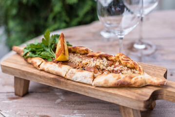 Boat-shaped Flatbread Pide Filled with Ground Meat Served with Fresh Herbs and Lemon Wedge