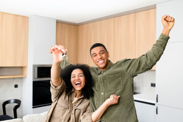 Multiracial couple in love hugging in a new home while holding keys in hands. Young multiracial family bought a new house, rent an apartment, got a mortgage
