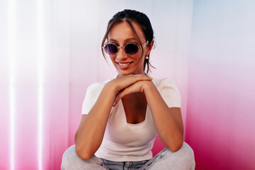 Close up studio shot of smiling stylish lady in sunglasses smiling at camera while posing in bright studio 