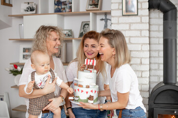 Portrait of delightful family three women congratulating baby infant looking at cake, celebrating...
