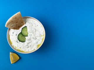 Traditional greek sauce tzatziki in a white bowl on blue background