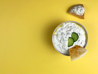 Traditional greek sauce tzatziki in a white bowl on yellow background