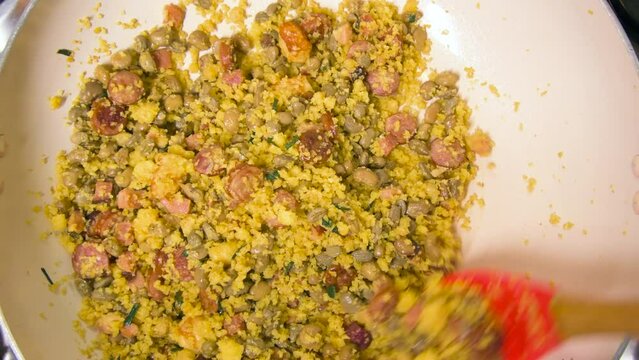 Cooking and mixing with a spoon the Northeastern Feijao Tropeiro, brazilian dish made with cuscuz, string bean, sausage, bacon, chive and curd cheese. 