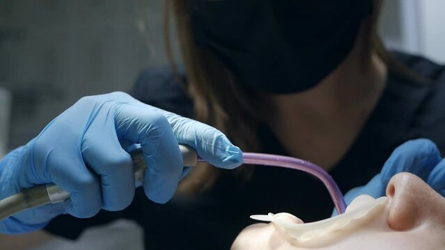 Young female dentist in blue latex gloves brushing the patient's teeth with a jet of water and a saliva ejector
