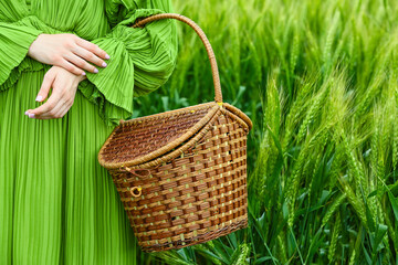 Woman with wicker basket in green wheat field