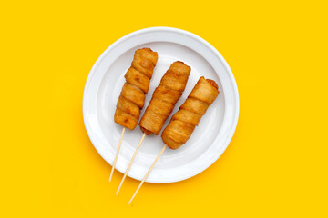 Fried dough snacks wrapped sausage in plate on yellow background.