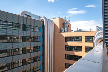 Metal ventilation pipes on the outer wall of modern office building against a blue sky background.