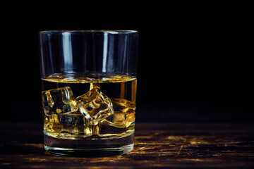 Glass chilled whiskey with ice cubes on wooden background in cellar.