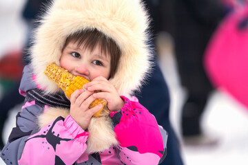 Portrait of a little girl in winter clothes with an ear of corn at her mouth.