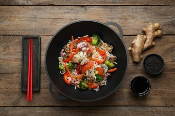 Stir fried noodles with seafood and vegetables in wok on wooden table, flat lay
