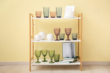 Different glasses, decor and books on shelf unit near color wall