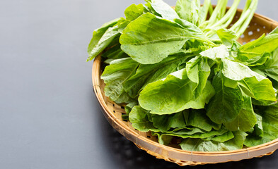 Green spinach in bamboo basket on dark background.
