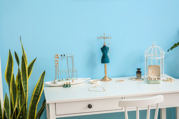 Fototapeta premium Stands and box with stylish jewelry on white table near blue wall