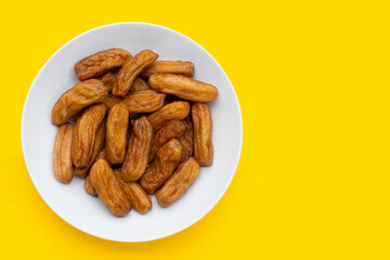 Sun-dried bananas in white plate on yellow background.
