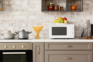 Modern microwave oven on counter near light brick wall in kitchen - obrazy, fototapety, plakaty