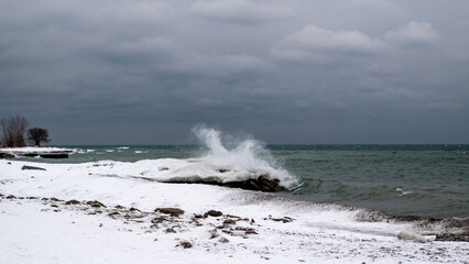 Fototapeta na wymiar Waves crash dramtically in to an ice berm on the shore of Lake Ontario in winter.
