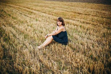 Naklejka na ściany i meble A beautiful girl and a field on which they threshed grain. Woman after harvest. Girl and yellow field 