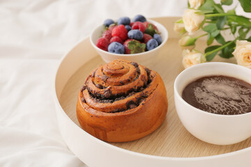 Tray with delicious breakfast and flowers on bed, closeup