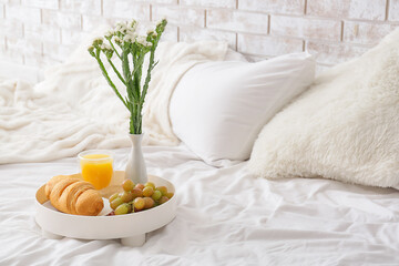 Obraz na płótnie Canvas Tray with breakfast and vase with flowers on bed