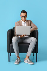 Young man using laptop in leather armchair on blue background
