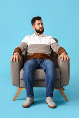 Handsome bearded man sitting in soft armchair on blue background