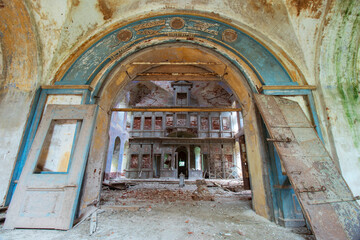The ruined blue entrance with a semicircular arch to the middle part of the old destroyed and abandoned Orthodox church in Russia. The destroyed iconostasis is visible. Broken doors. Peeling paint and