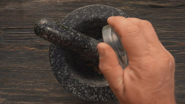 Top view of the male hands putting spices into the grey stone mortar