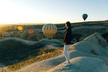 Young woman watching the sunrise and hot air balloons taking off over valley in Cappadocia, Goreme,...