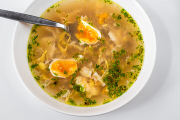 Golden poultry soup with poached egg in plate.
