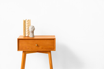 Wooden bedside table with books and decor near light wall