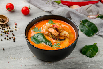 Tom Yam soup with seafood on black bowl on grey wooden table