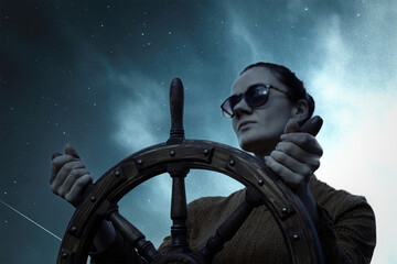 The girl controls the yacht, hands on the steering wheel,  handwheel on sky background © alzay