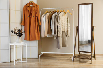 Fototapeta premium Rack with clothes and vase with autumn branches in room