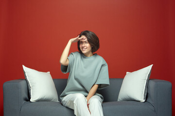 Young girl looking for something in distance, sitting on sofa on red background. Online store discounts, sale concept