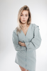 Stylish beautiful blonde woman with hairstyle in trendy denim clothes stands in the studio. Fashion girl