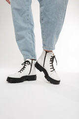 Fashionable woman with blue jeans in stylish leather white shoes with black laces and soles on a white background in the studio, close-up. Women's fashion and footwear. New collection 2021