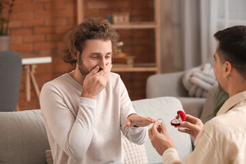 Young gay putting engagement ring on his boyfriend's finger at home