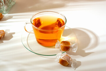 Transparent glass tea cup and a few caramel candies on light background. 