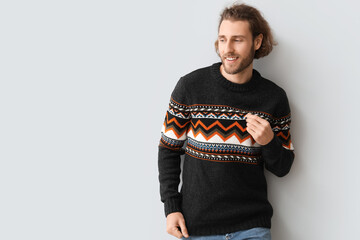 Handsome young man in knitted sweater on grey background