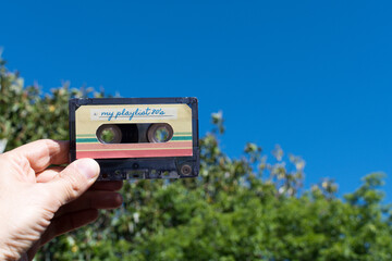 Hand holding a pair of audio cassette with the inscription my playlist 80's, outdoors
