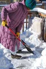 Mature female senior shoveling snow off patio deck outside.