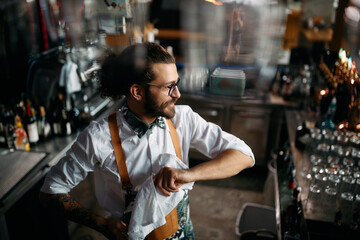 Happy man cleans drinking glasses while working as barista in pub.